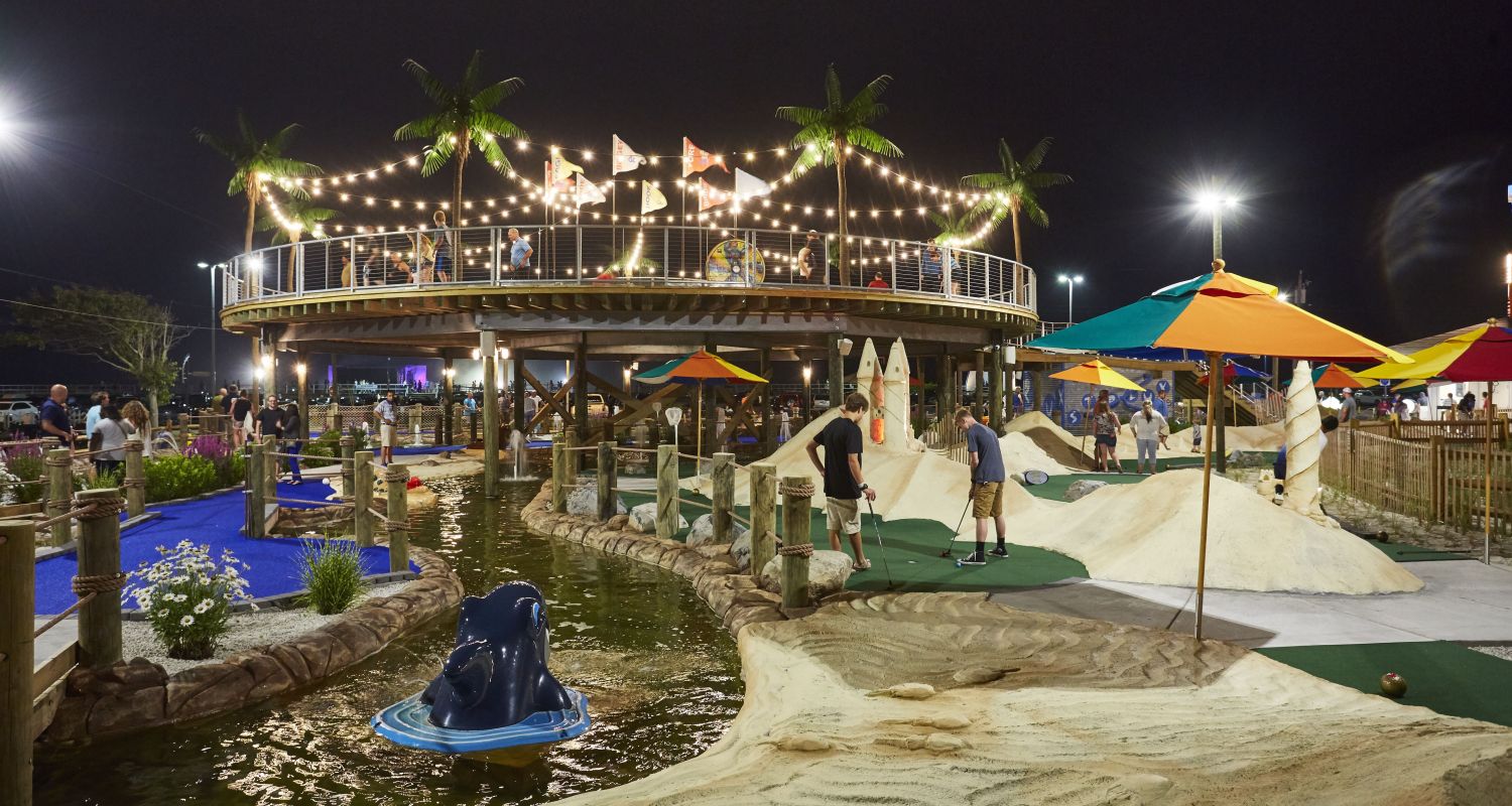 Players enjoying Starlux Mini Golf beside water features beneath evening string lights